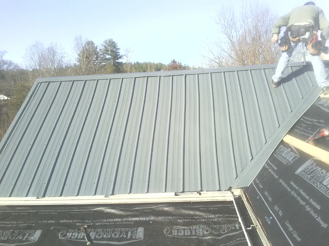 Crew installing dark green standing seam panels over synthetic underlayment in Black Creek
