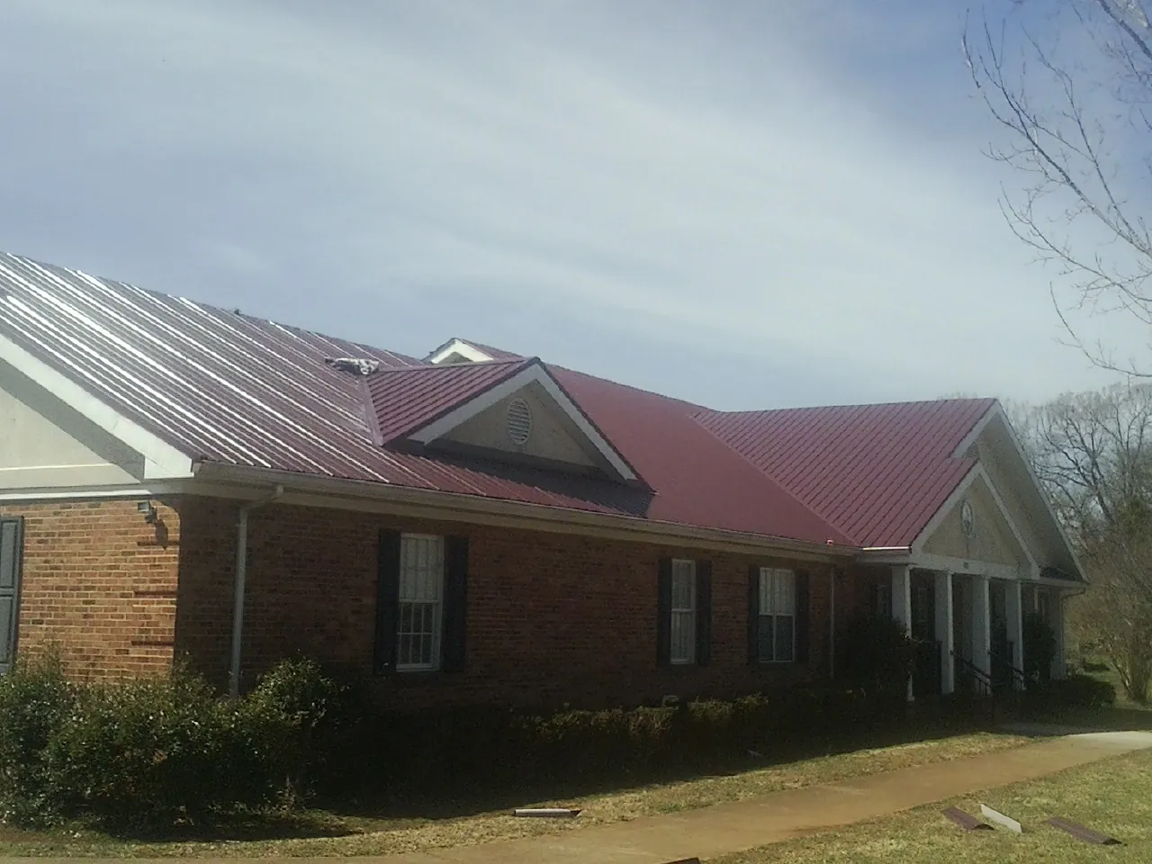 Red metal roof with gabled entries on a long brick building, from a Hail Damage Roof Repair job in Black Creek