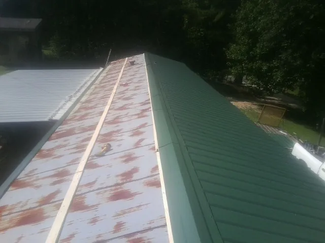 Old rusted panels beside newly installed green metal roofing — Wind Damage Roof Repair by Roofing Brothers in Black Creek