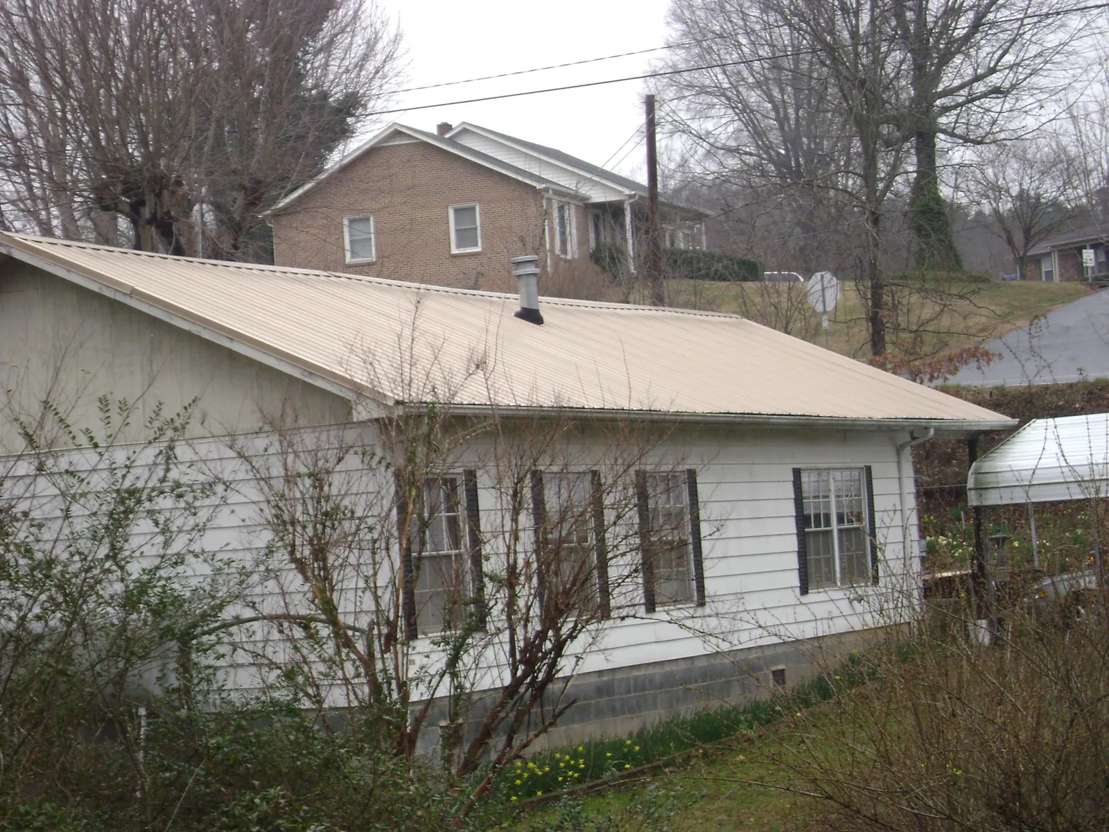 Tan metal roof on a white sided house set into a hillside — Commercial Roofing by Roofing Brothers in Black Creek